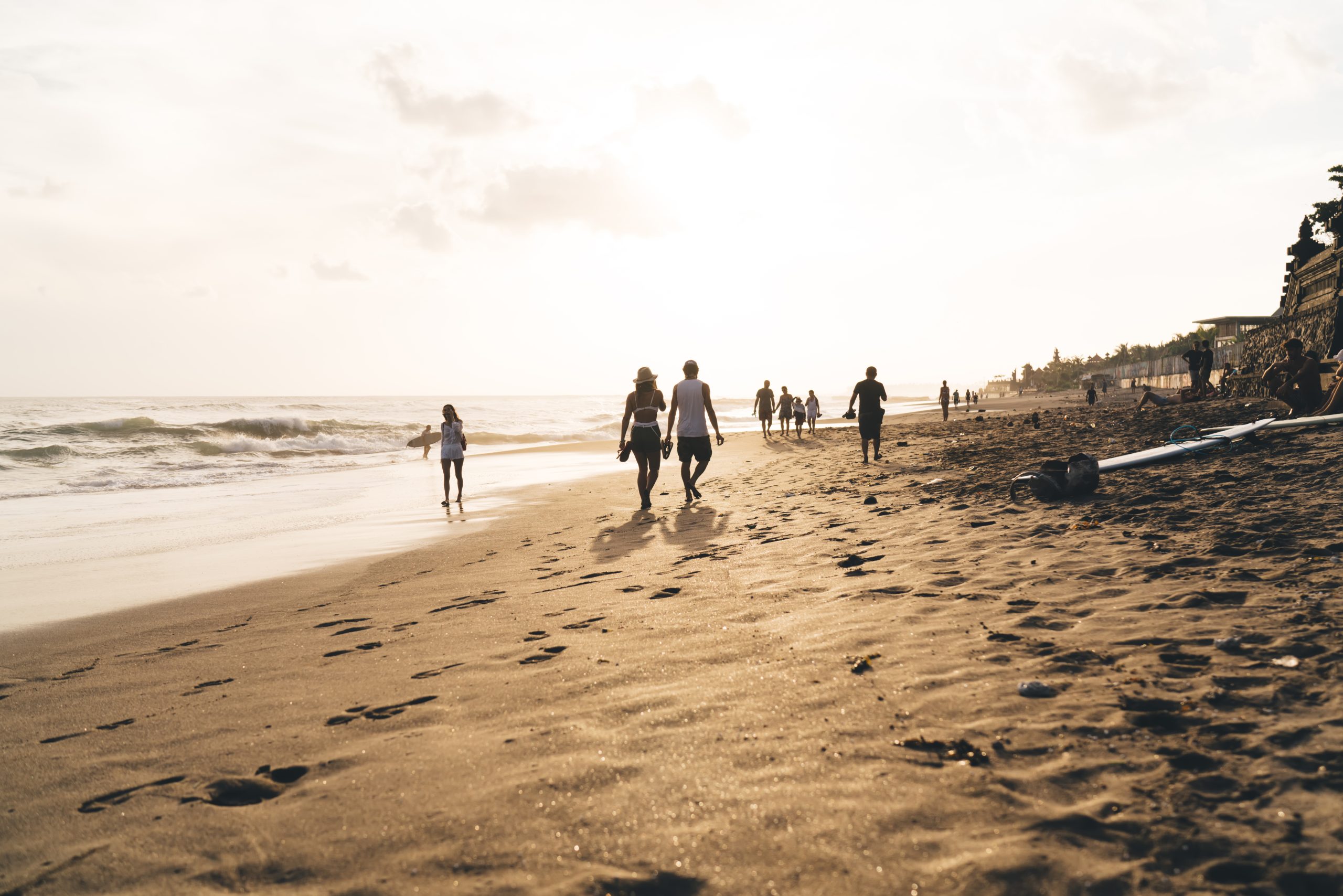 Tourists walking on sandy beach with falling sea waves nearby
